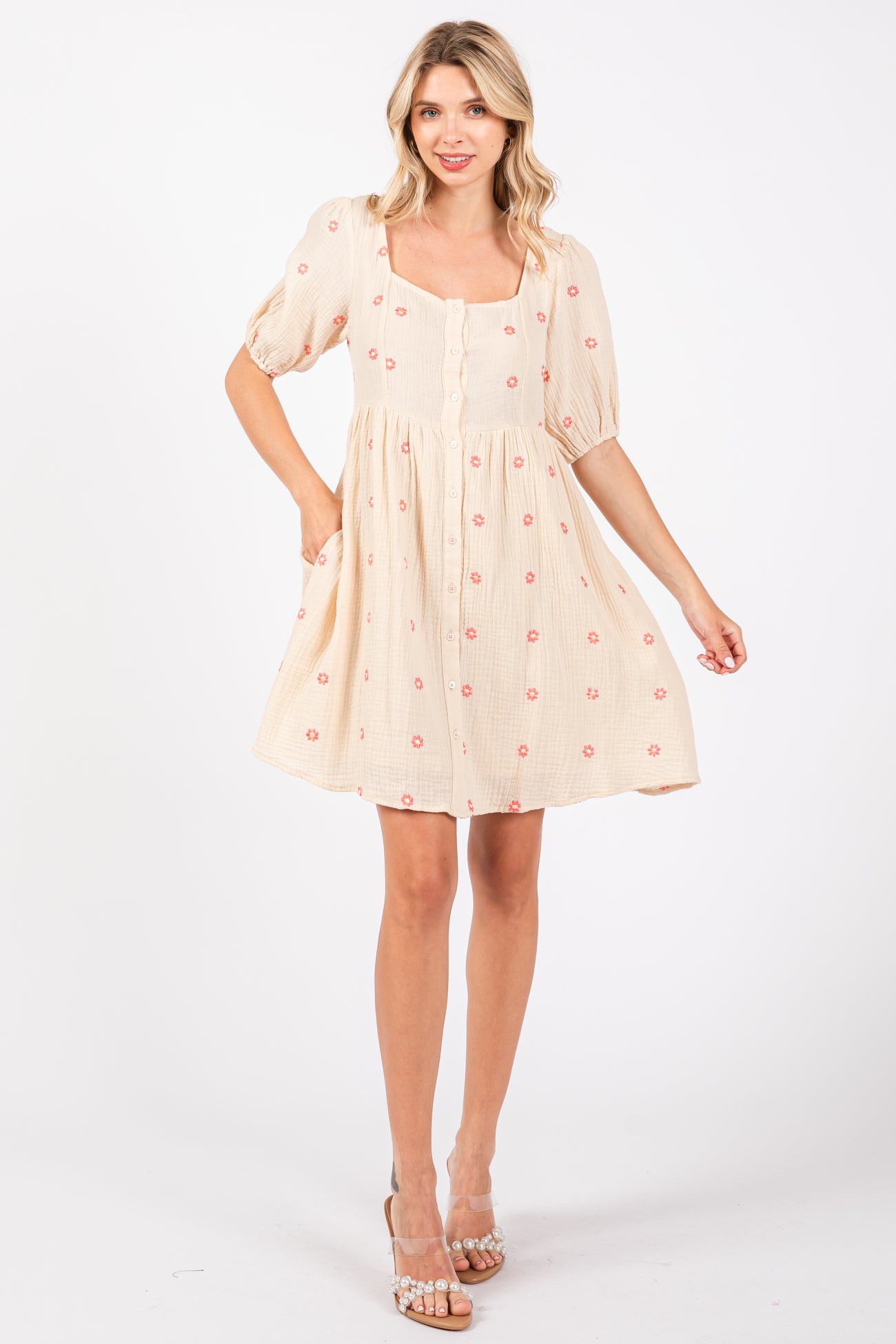 woman wearing a cream short sleeve dress with floral embroidery and a square neckline, standing and smiling