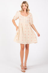 woman wearing a cream short sleeve dress with floral embroidery and a square neckline, standing and smiling