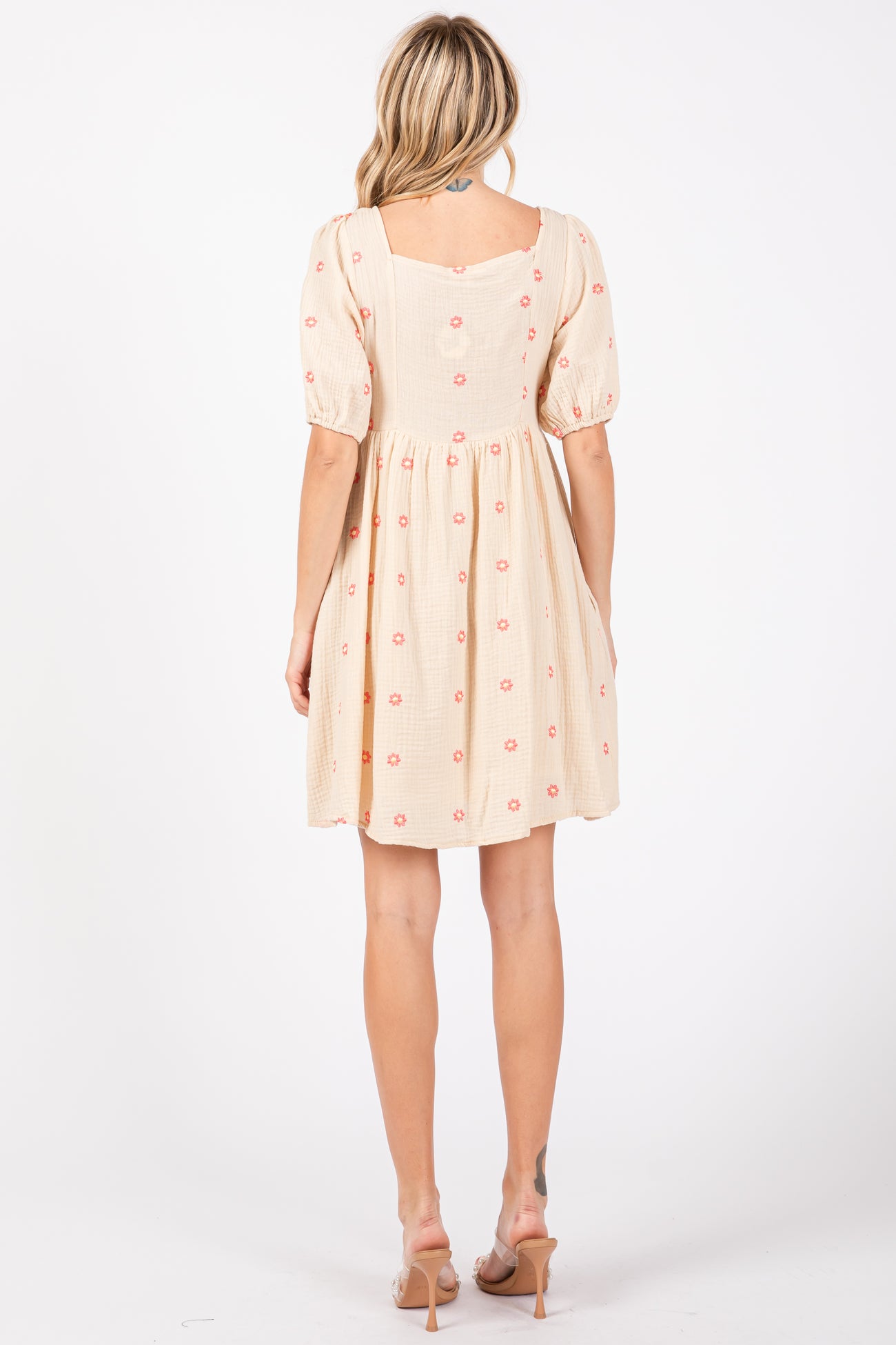woman wearing a light beige short dress with puff sleeves and floral embroidery, shown from the back