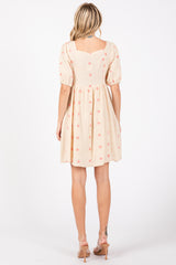 woman wearing a light beige short dress with puff sleeves and floral embroidery, shown from the back