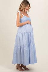 woman wearing a light blue maternity dress with tiered skirt and shoulder ties, gently holding her baby bump