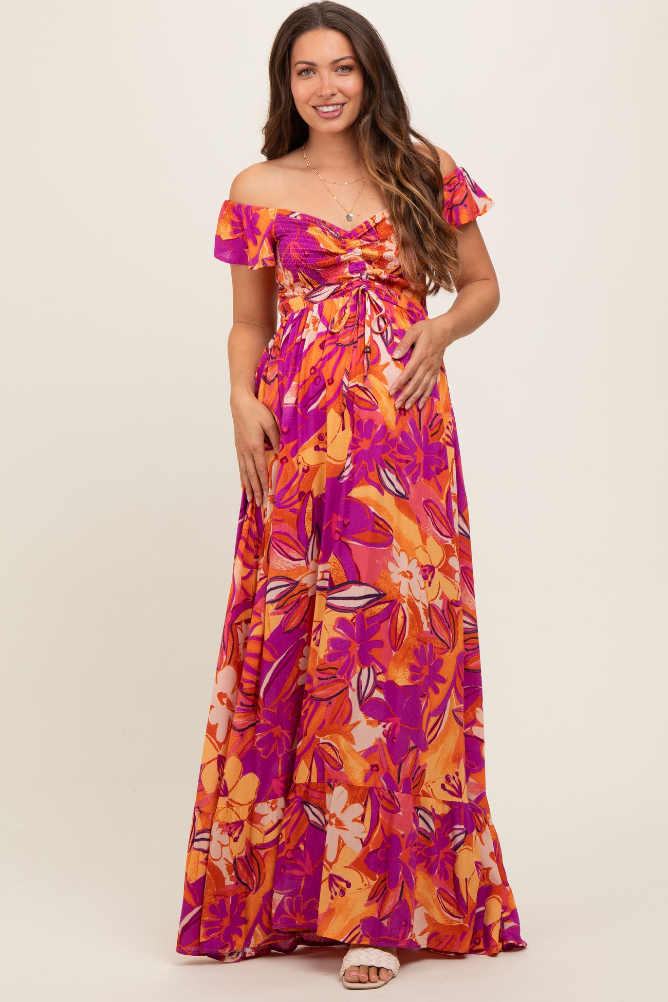 woman wearing a colorful off-shoulder floral maternity maxi dress with a gathered bodice and flowing skirt, highlighting her baby bump