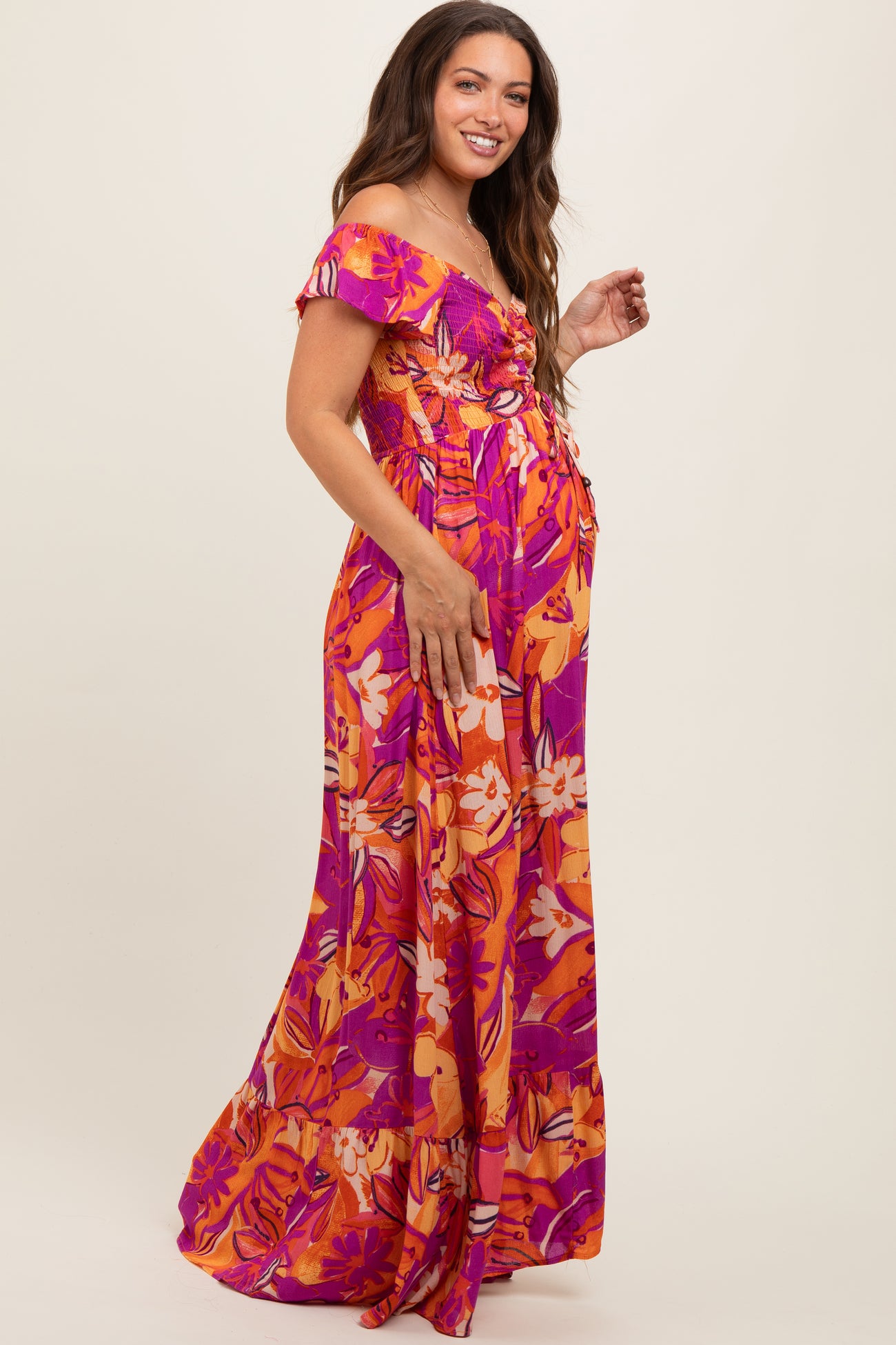 woman wearing a vibrant floral off-shoulder maternity dress with a flowing skirt and visible baby bump