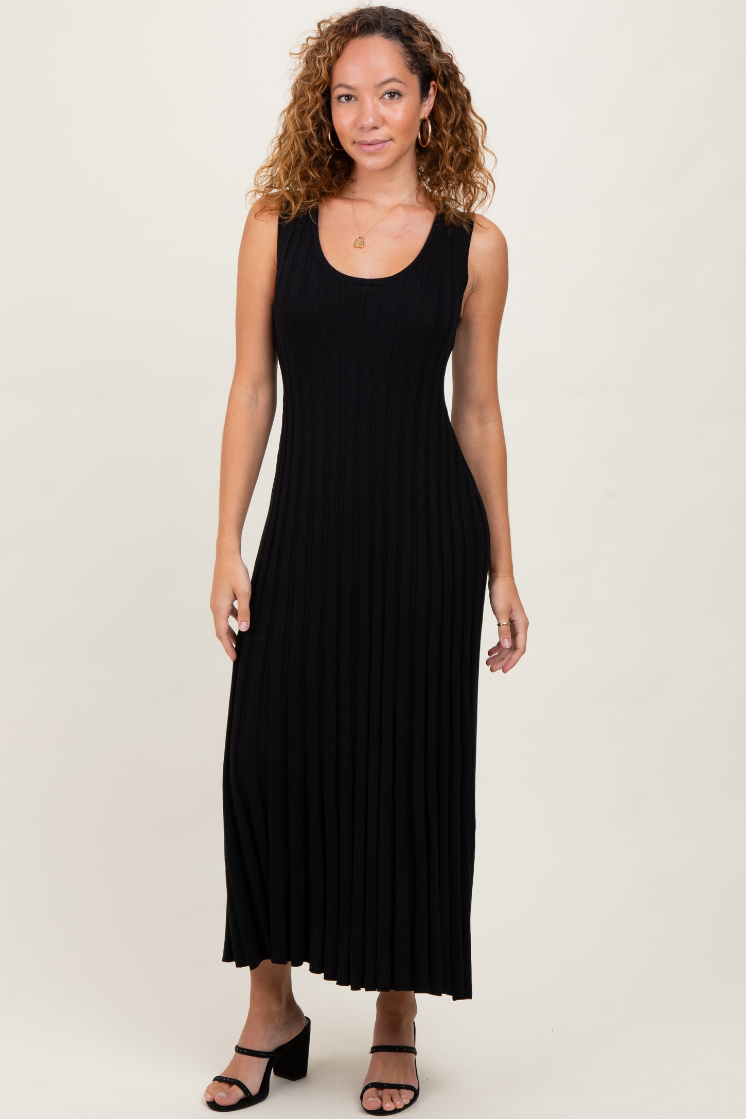 woman wearing a black ribbed maxi dress with a fitted bodice and flared skirt, posing in a neutral background