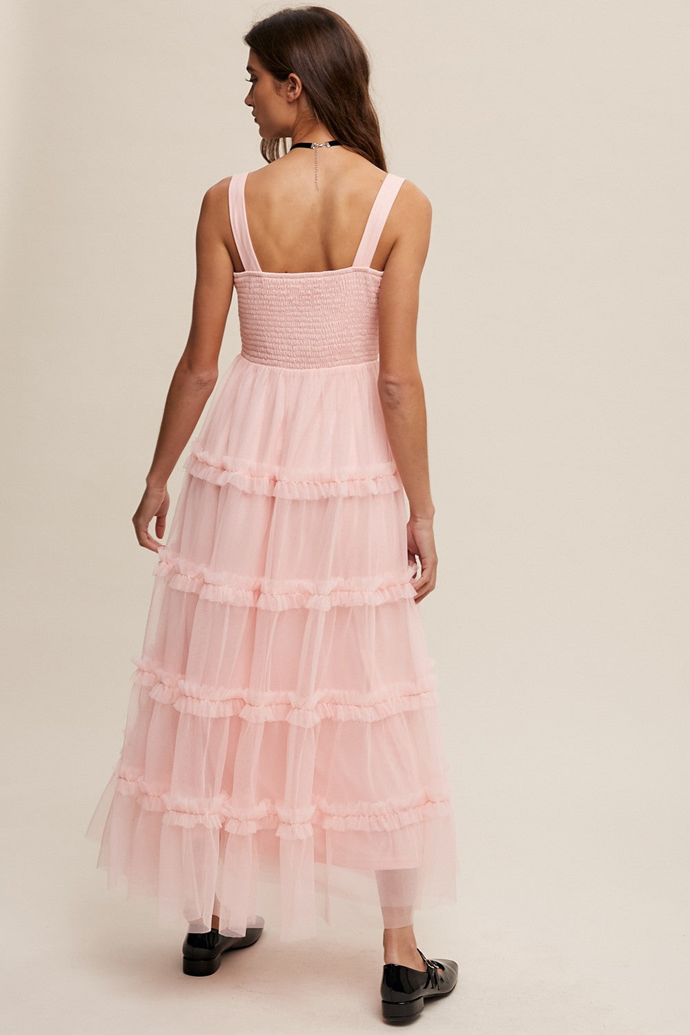 woman wearing a light pink tiered tulle maxi dress with a smocked bodice and wide straps, viewed from the back