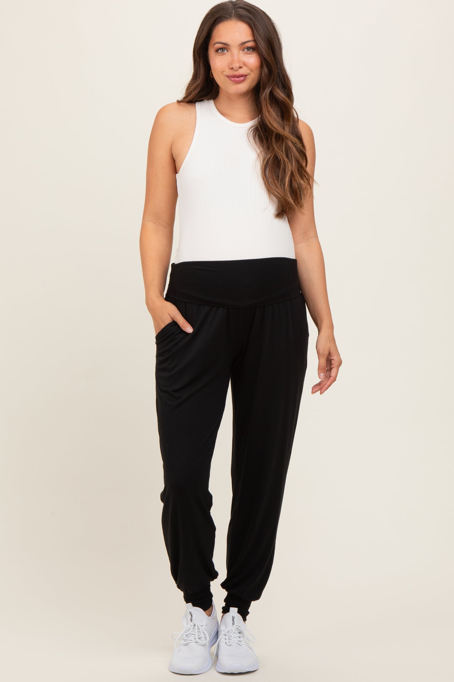 woman wearing black maternity joggers and a white sleeveless top, with pockets and elastic cuffs at the ankles