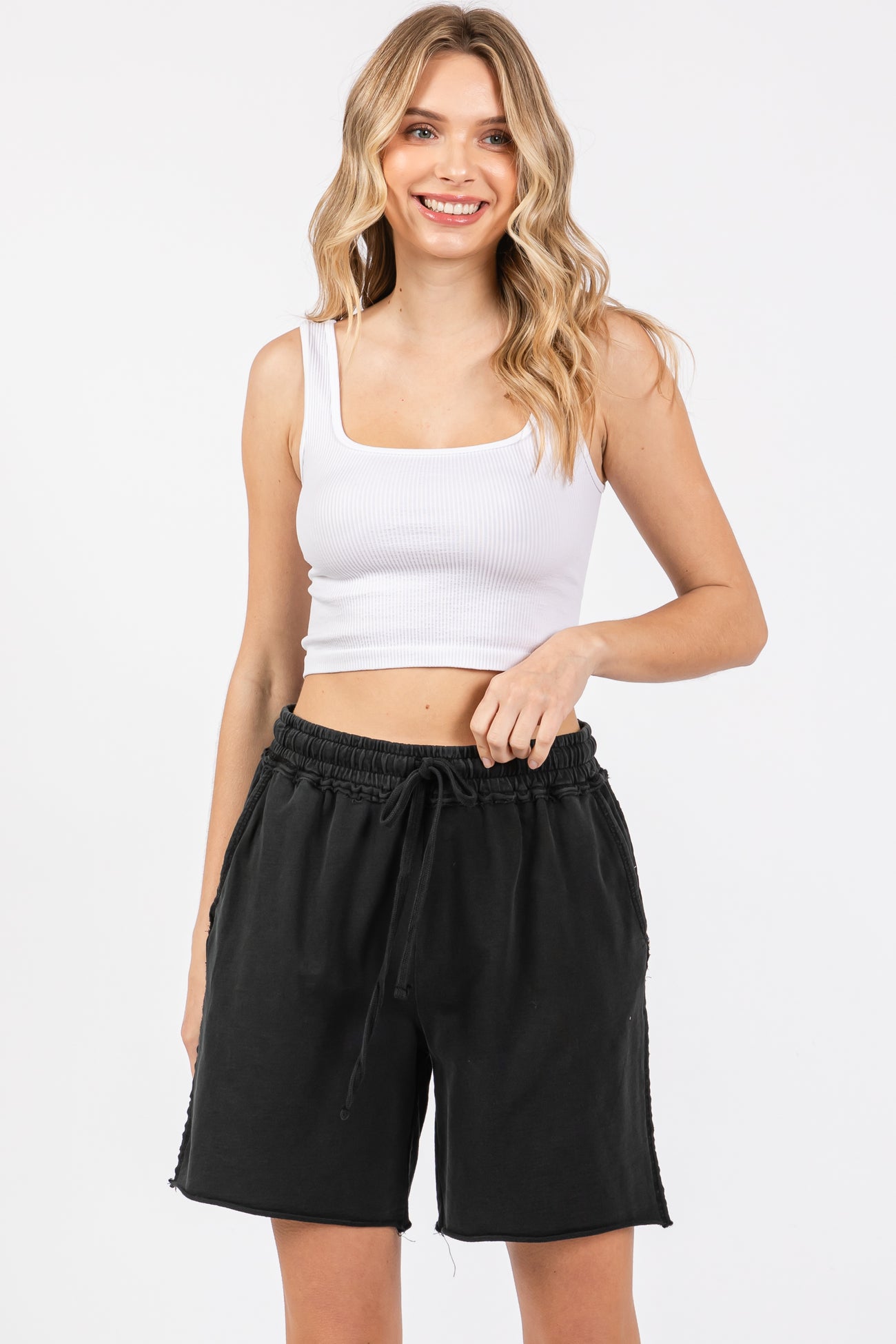 woman wearing a white ribbed crop top and black drawstring shorts, smiling at the camera