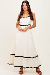 woman wearing a cream maxi dress with black ric rac trim and a fitted bodice