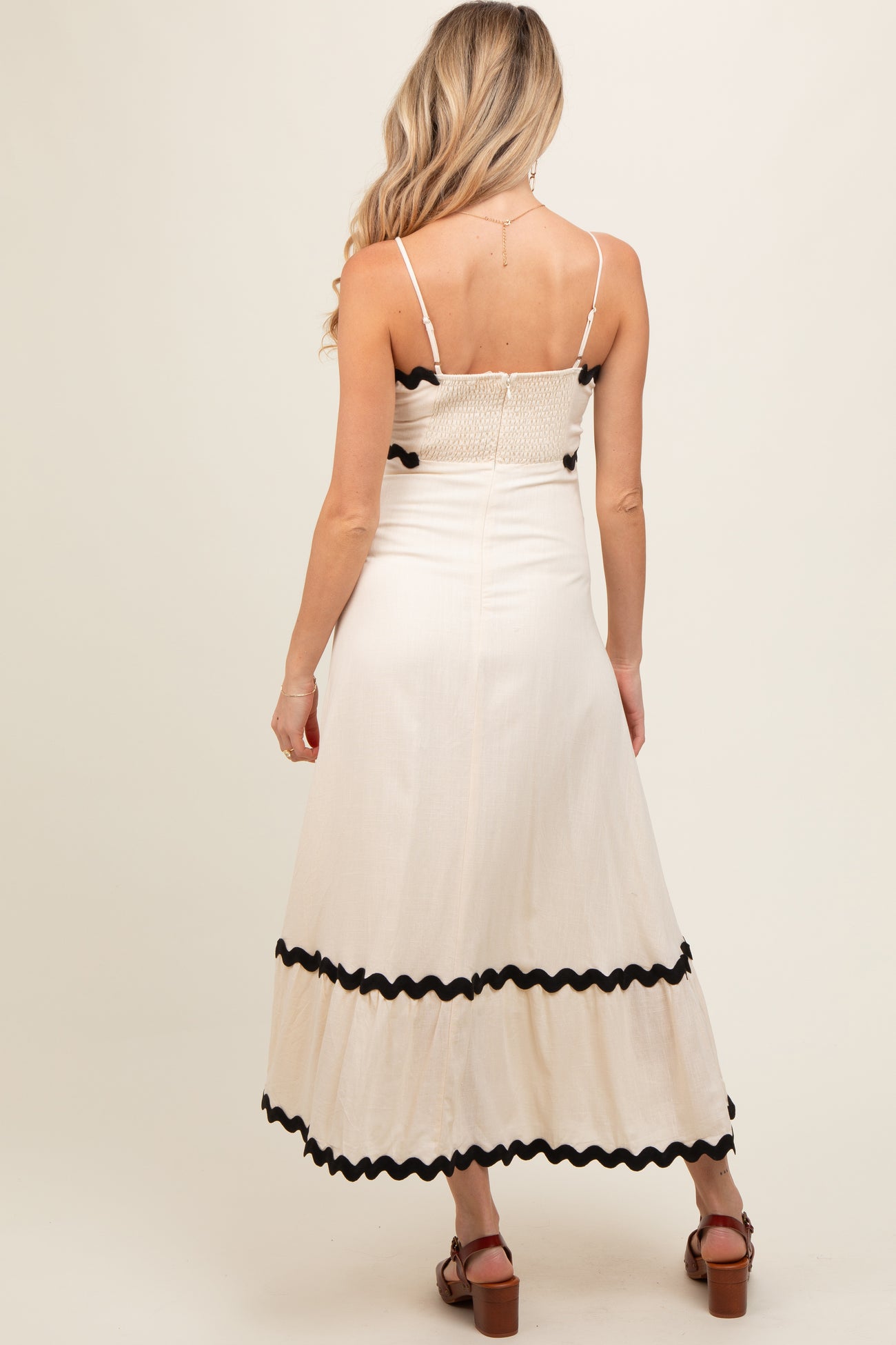 woman wearing a cream maternity maxi dress with black trim and a smocked bodice, showing a small baby bump