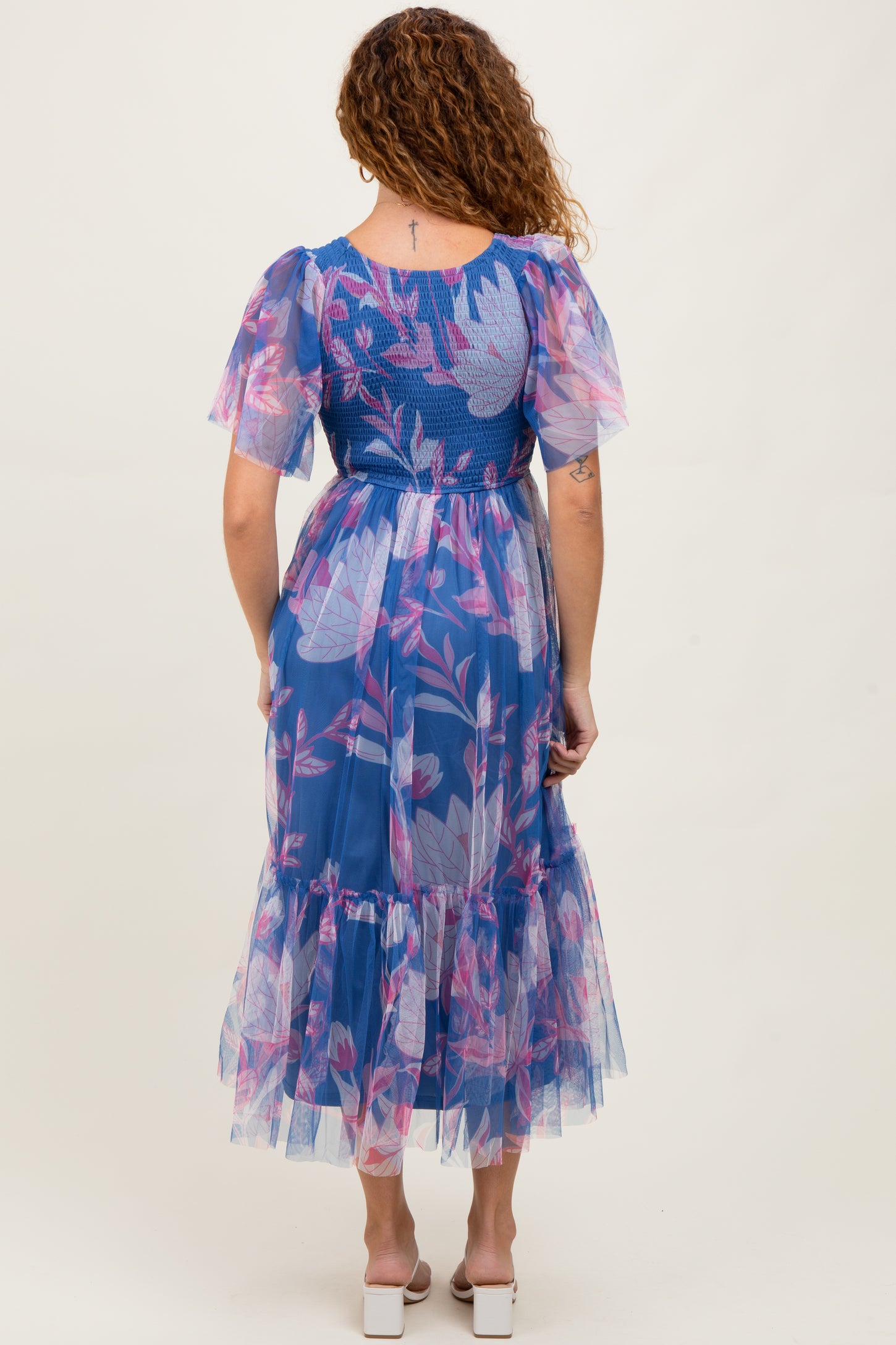 woman wearing a sheer blue floral maxi dress with puff sleeves and a ruffled hem, seen from the back