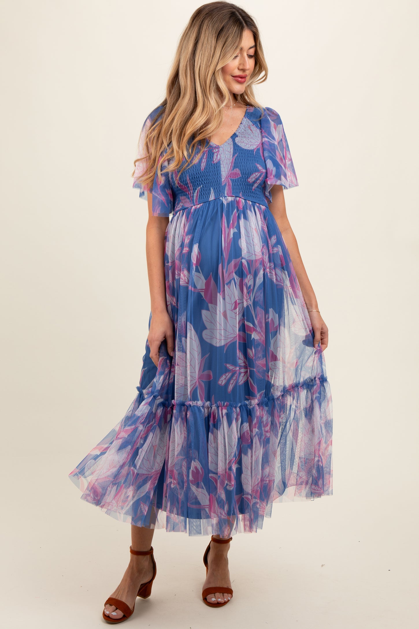 woman wearing a blue floral maternity dress with short flutter sleeves and a tiered skirt, showcasing her baby bump