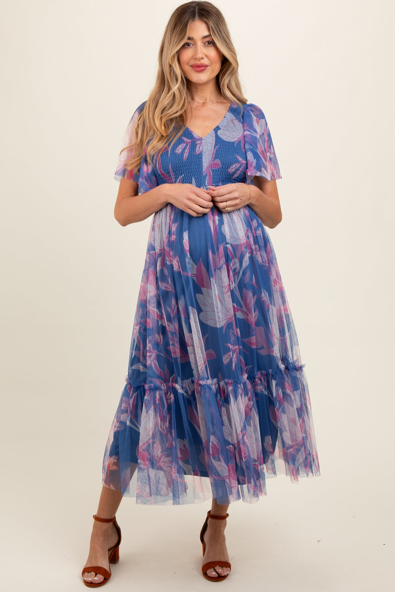 woman wearing a blue floral maternity dress with short sleeves and a tiered skirt, showcasing her baby bump