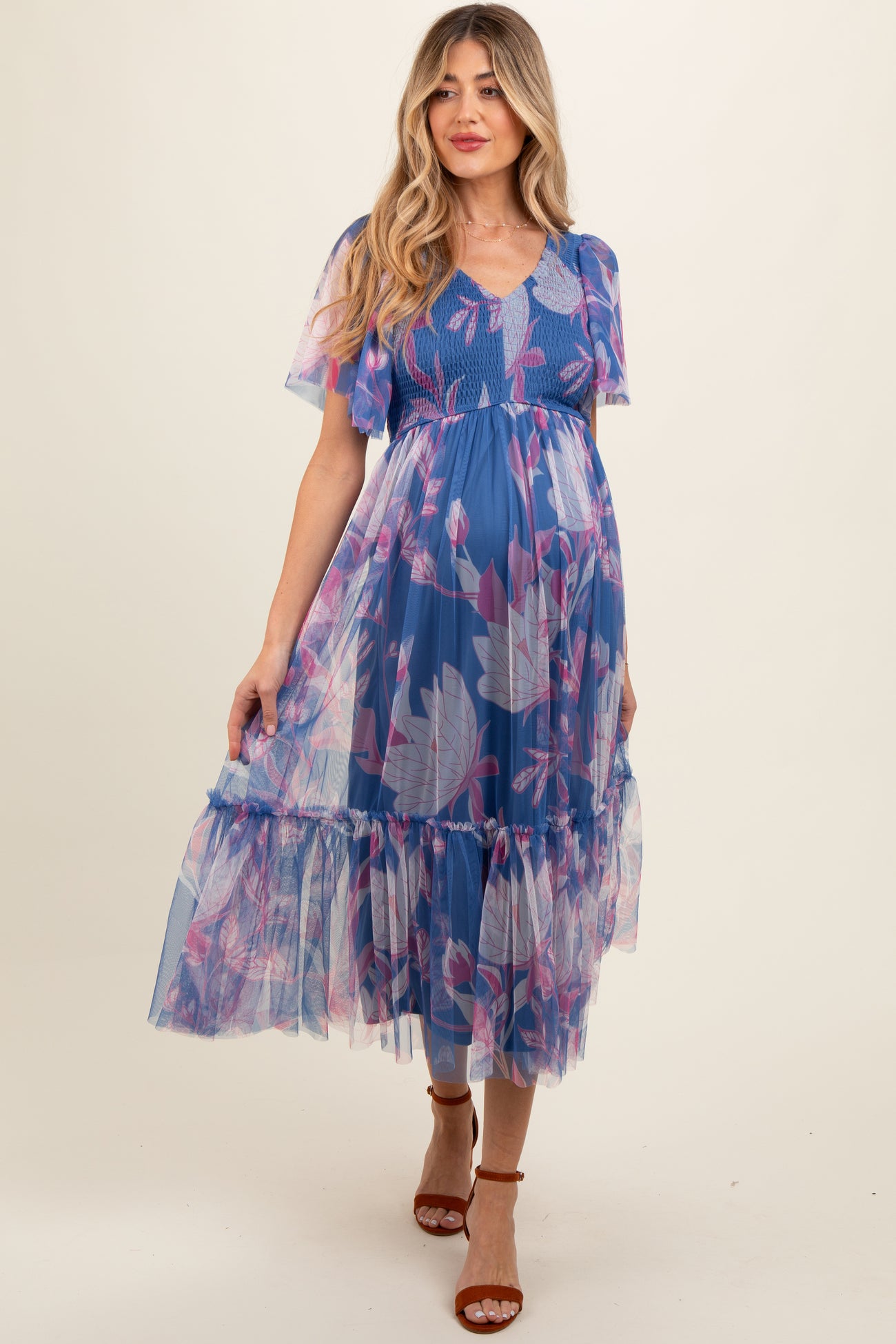 woman wearing a blue floral maternity dress with flutter sleeves and a tiered hem, showcasing her baby bump
