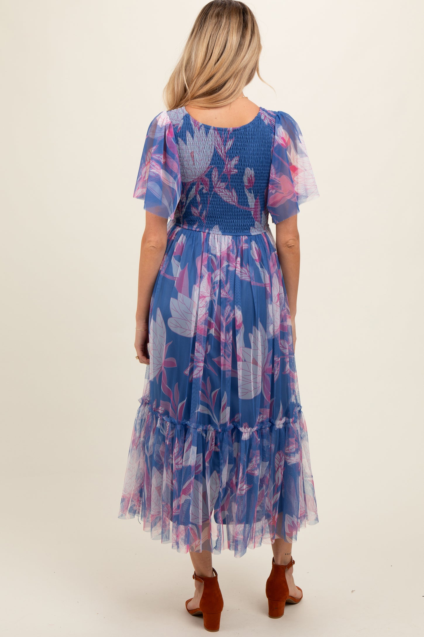 woman wearing a blue floral maternity dress with flutter sleeves and a layered skirt, showing a baby bump from the back