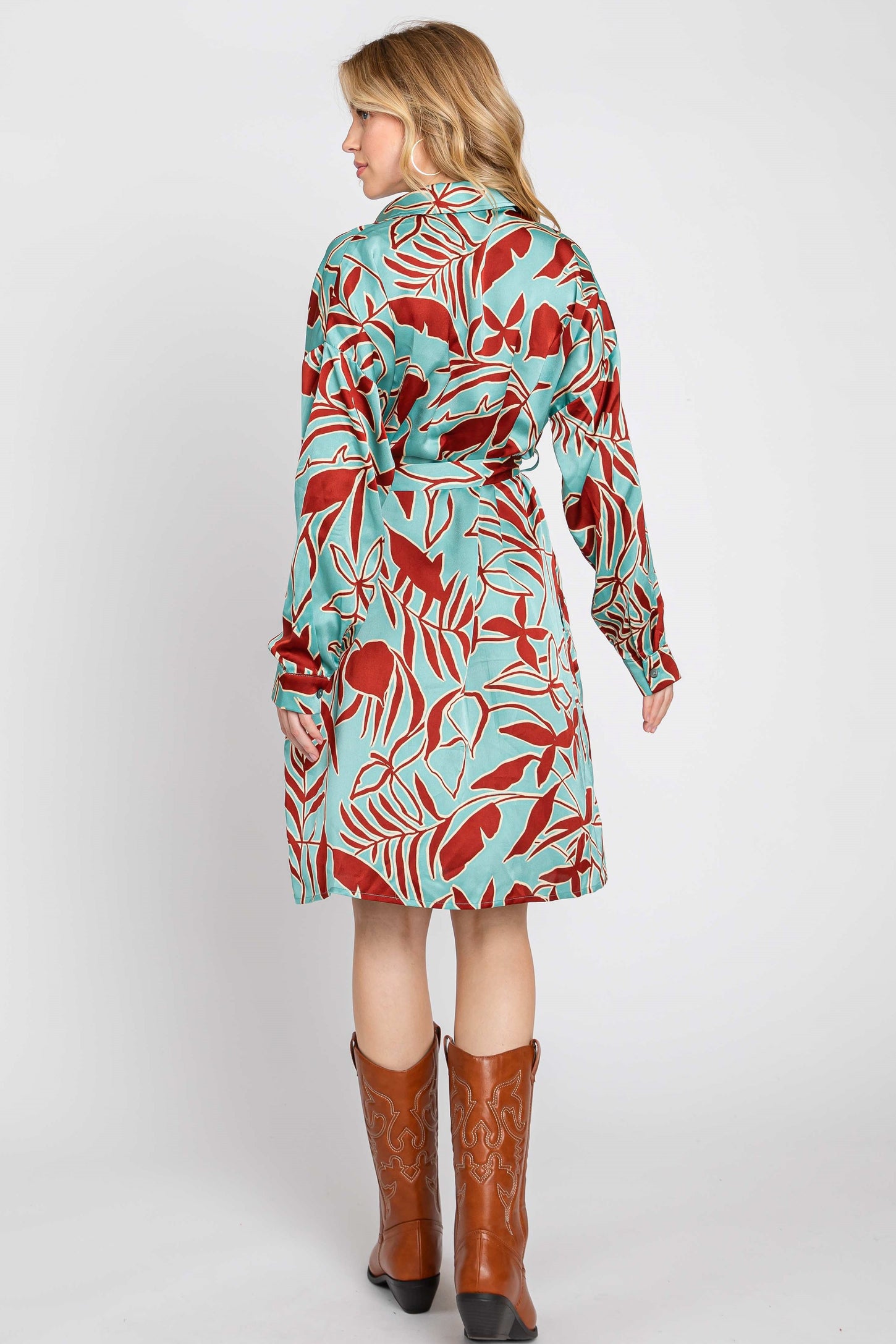 woman wearing a long sleeve turquoise dress with red floral print and a tie belt, paired with brown cowboy boots