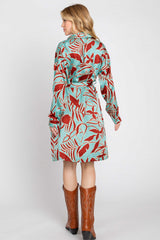 woman wearing a long sleeve turquoise dress with red floral print and a tie belt, paired with brown cowboy boots