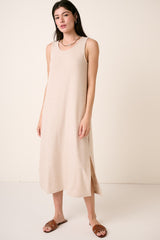 woman wearing a beige sleeveless maxi dress with side slits and brown slide sandals