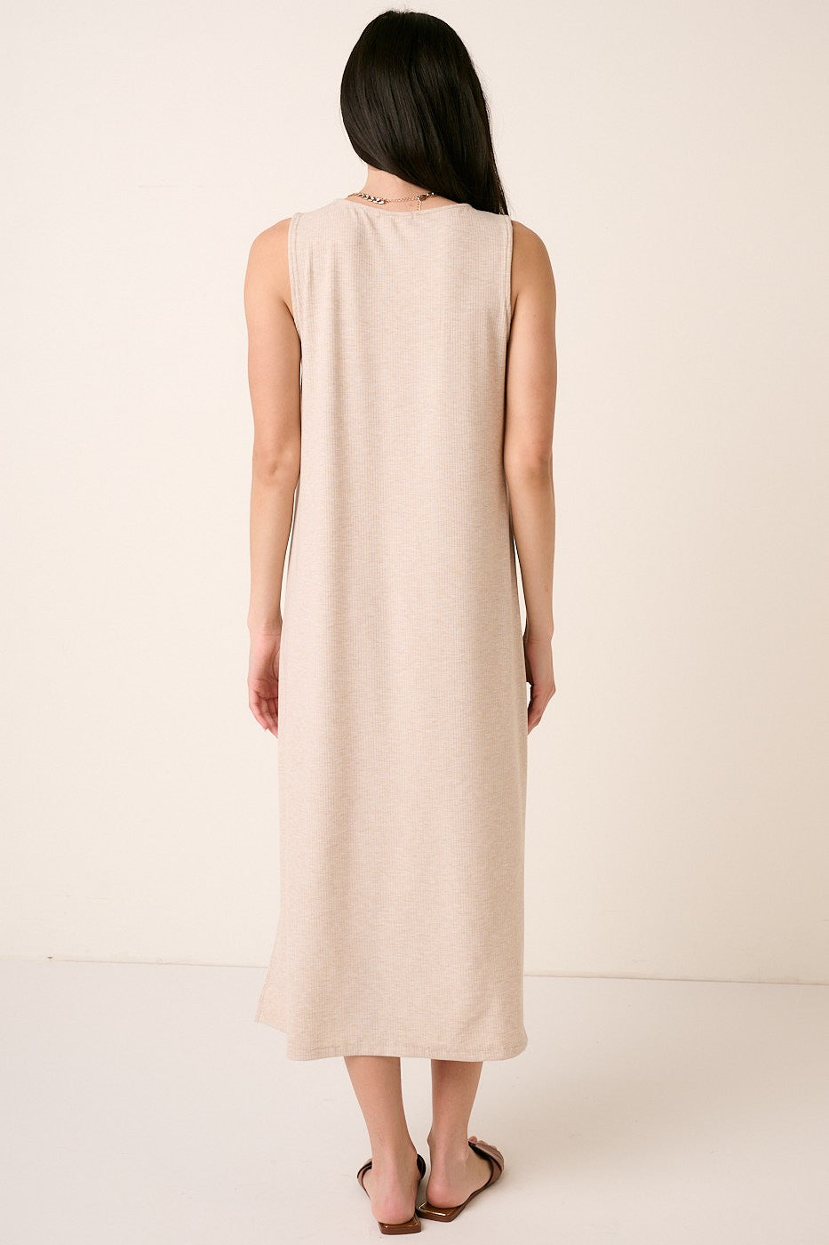 woman wearing a long beige sleeveless maxi dress, viewed from the back, with a relaxed fit and simple design