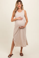 woman wearing a beige sleeveless maternity dress with side slits, holding her baby bump and smiling