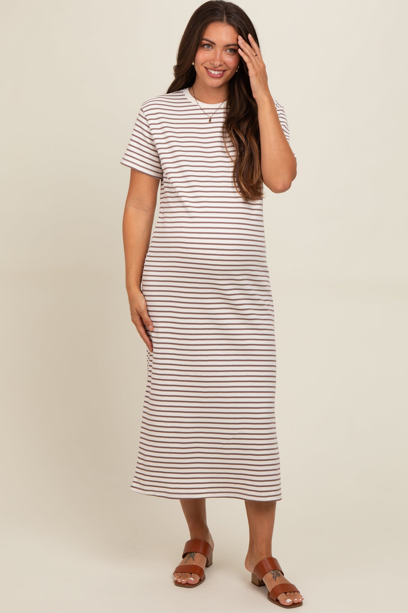 woman wearing a striped midi maternity dress with short sleeves and a relaxed fit, gently touching her hair