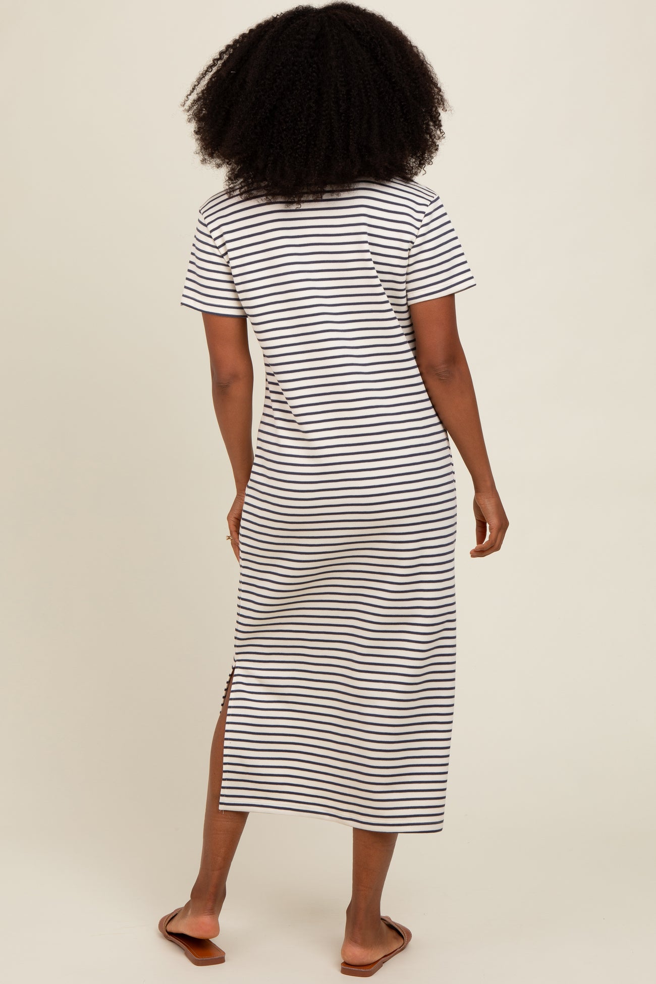 woman wearing a black and white striped maxi dress with short sleeves and side slits, viewed from the back