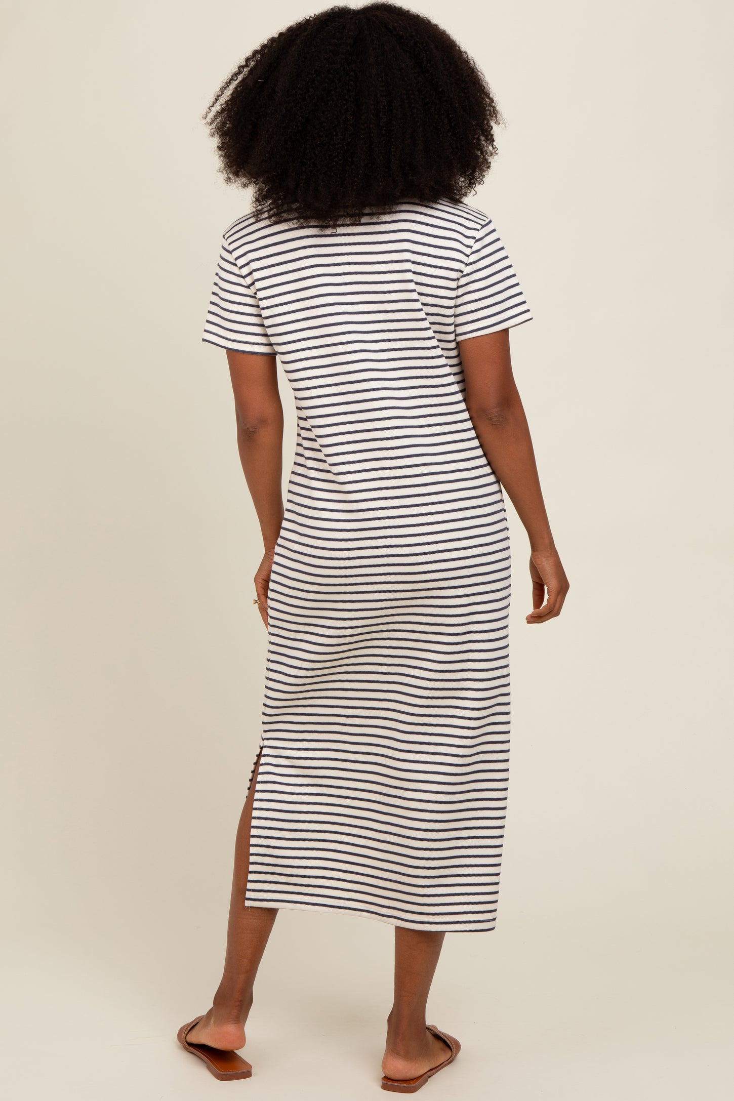 woman wearing a black and white striped maxi dress with short sleeves and side slits, viewed from the back