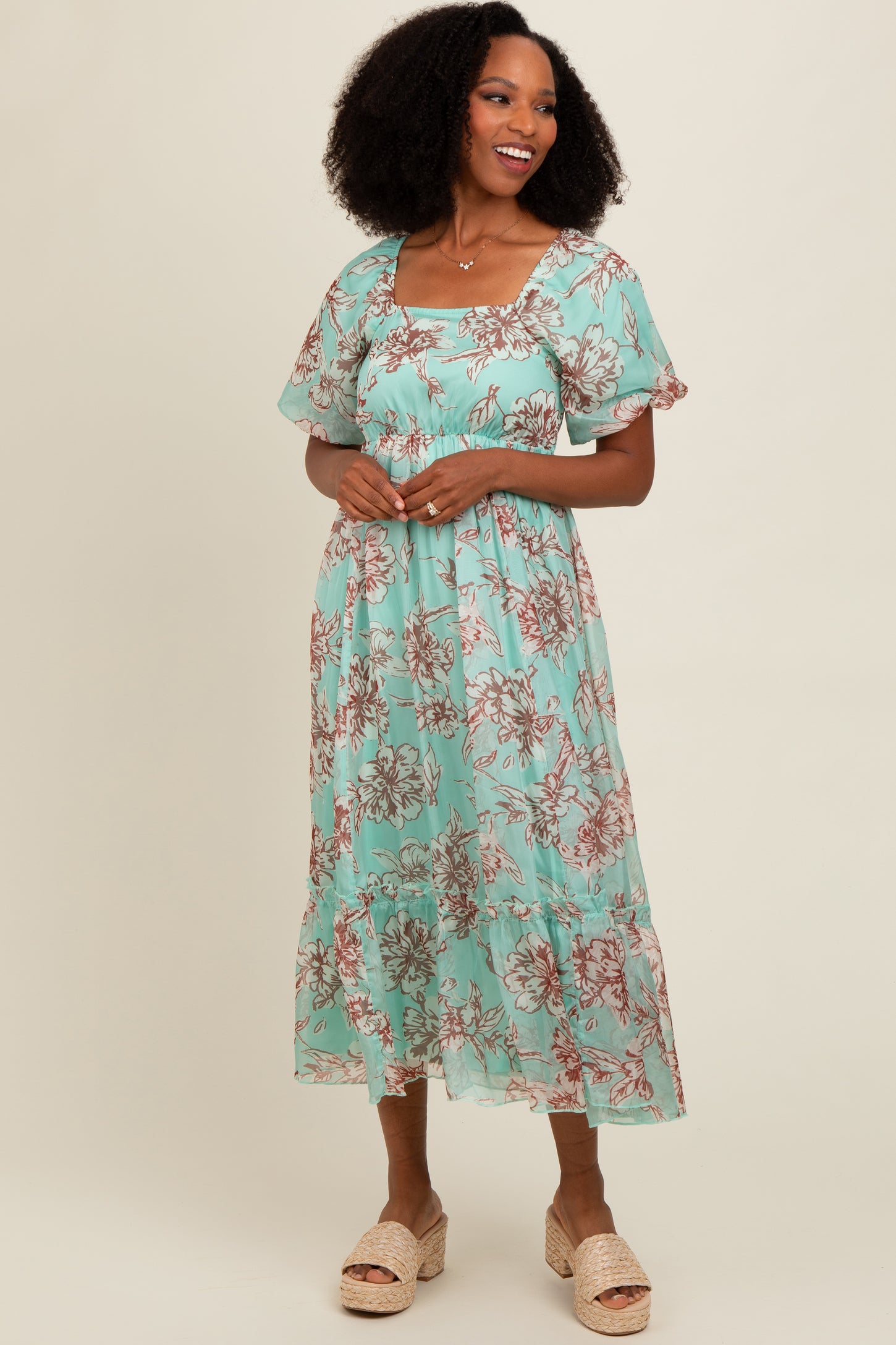 woman wearing a mint green floral midi dress with short puff sleeves and a tiered skirt, smiling against a plain background