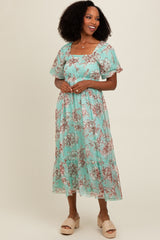 woman wearing a mint green floral midi dress with short puff sleeves and a tiered skirt, smiling against a plain background