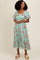 woman wearing a mint green floral midi dress with short puff sleeves and a tiered skirt, smiling against a plain background