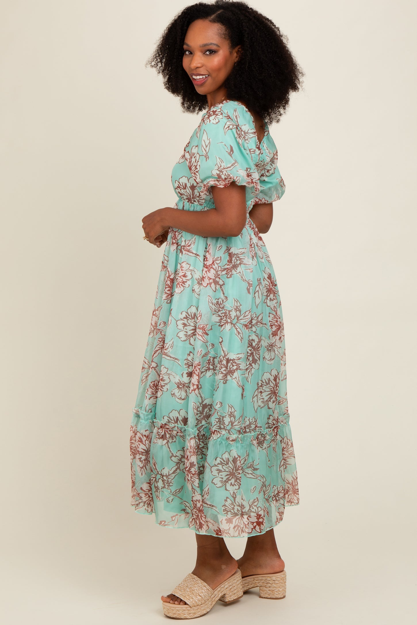 woman wearing a mint green floral maxi dress with puff sleeves and a tiered hem, standing sideways