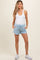 woman wearing a white tank top and light blue maternity shorts with pockets, styled with white sneakers