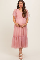 woman wearing a pastel pink maternity dress with flutter sleeves and tiered tulle fabric, holding her baby bump