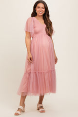 woman wearing a pink maternity dress with puff sleeves and a tiered tulle skirt, displaying her baby bump