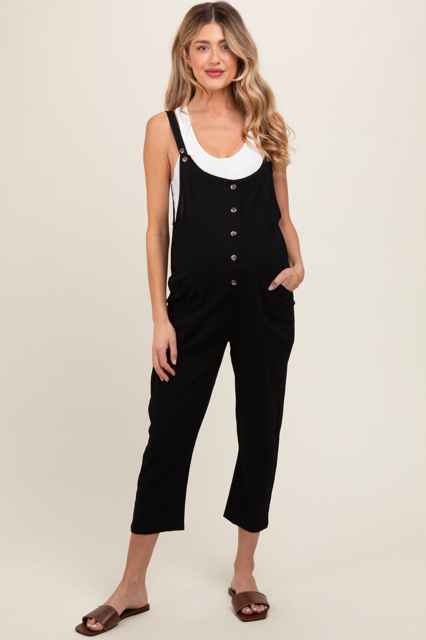 woman wearing a black maternity jumpsuit with buttons and pockets, standing and showing her baby bump