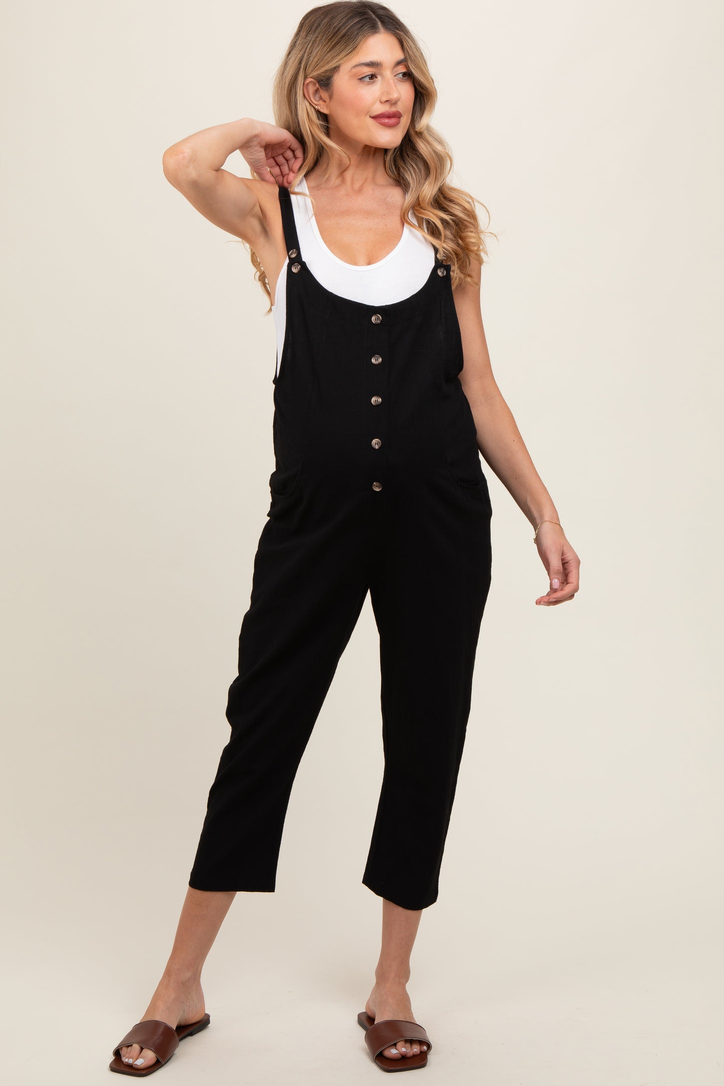 woman wearing a black maternity overall jumpsuit with buttons and pockets, showing off her baby bump