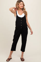 woman wearing a black maternity overall jumpsuit with buttons and pockets, showing off her baby bump