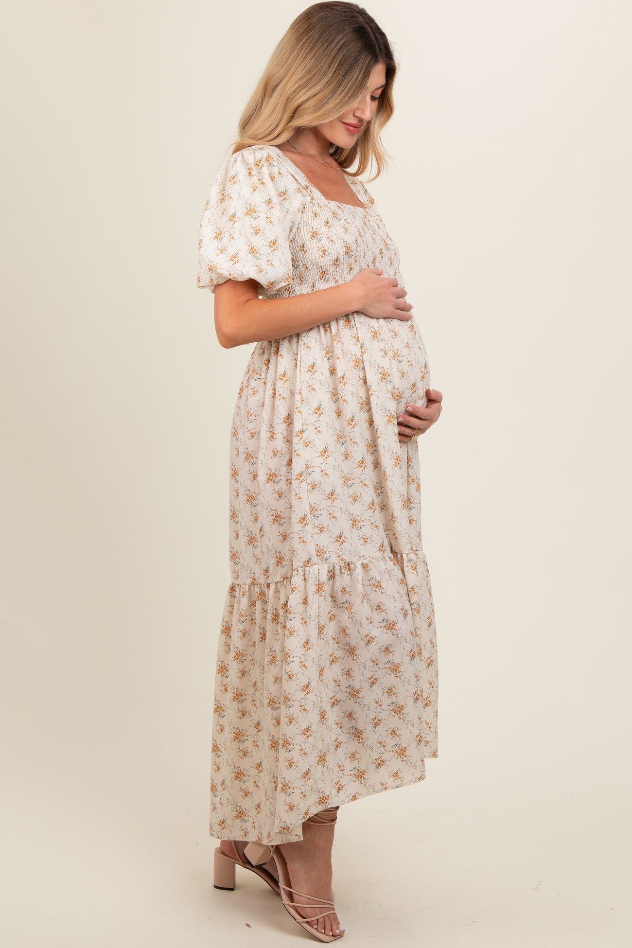 woman wearing a cream floral maternity maxi dress with puff sleeves and a tiered skirt, highlighting her baby bump