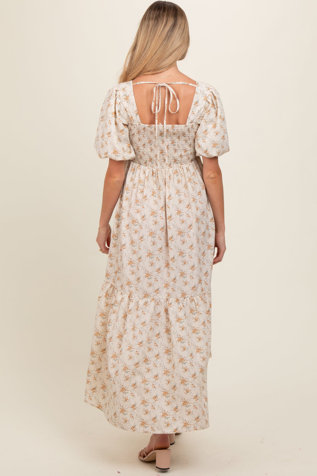 woman wearing a floral maxi maternity dress with puff sleeves and a smocked back, showcasing a tie detail