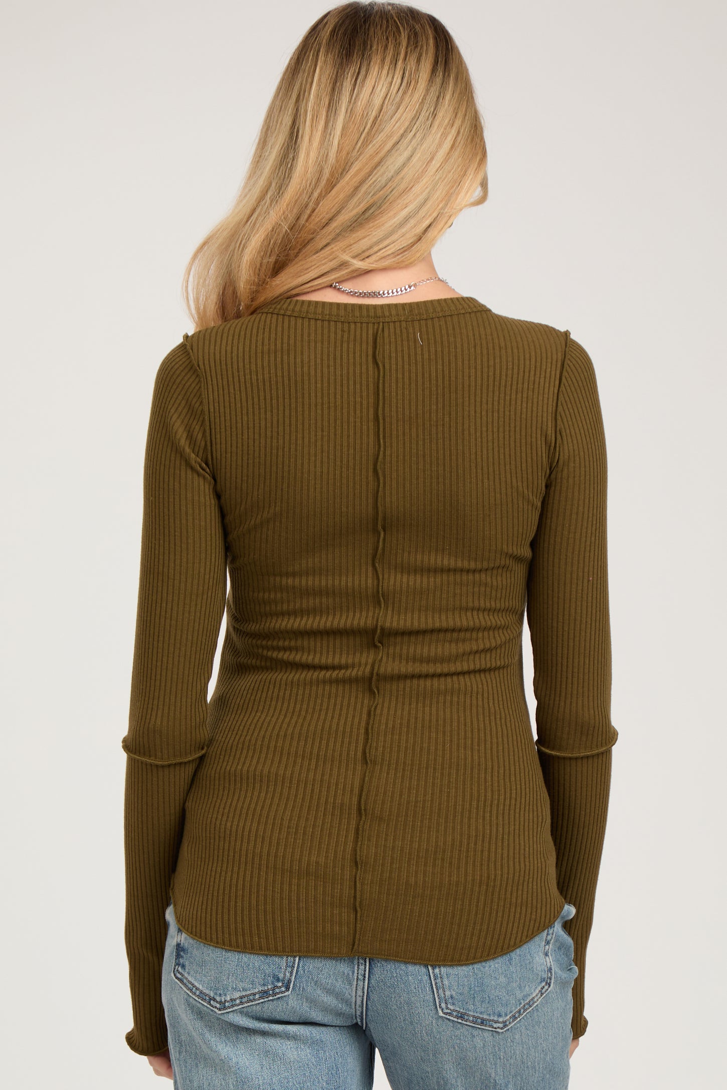 woman wearing a ribbed olive green maternity top, view from the back, with long sleeves and curved hem