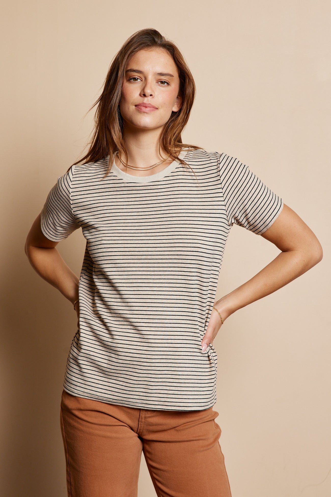 woman wearing a striped short sleeve top in beige and brown with hands on hips