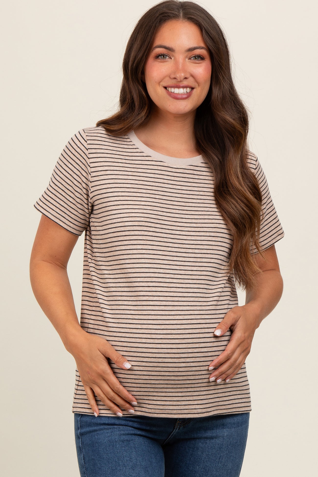 woman wearing a light brown and cream striped maternity top and holding her baby bump