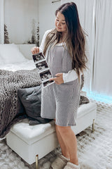 woman wearing a striped maternity dress holding ultrasound photos and looking at them while standing in a cozy bedroom setting