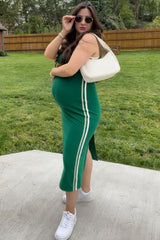 woman wearing a green maternity dress with side stripes and a baby bump, accessorized with sunglasses and a white bag