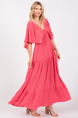 woman wearing a coral maxi dress with flutter sleeves and a tiered skirt, standing in a relaxed pose