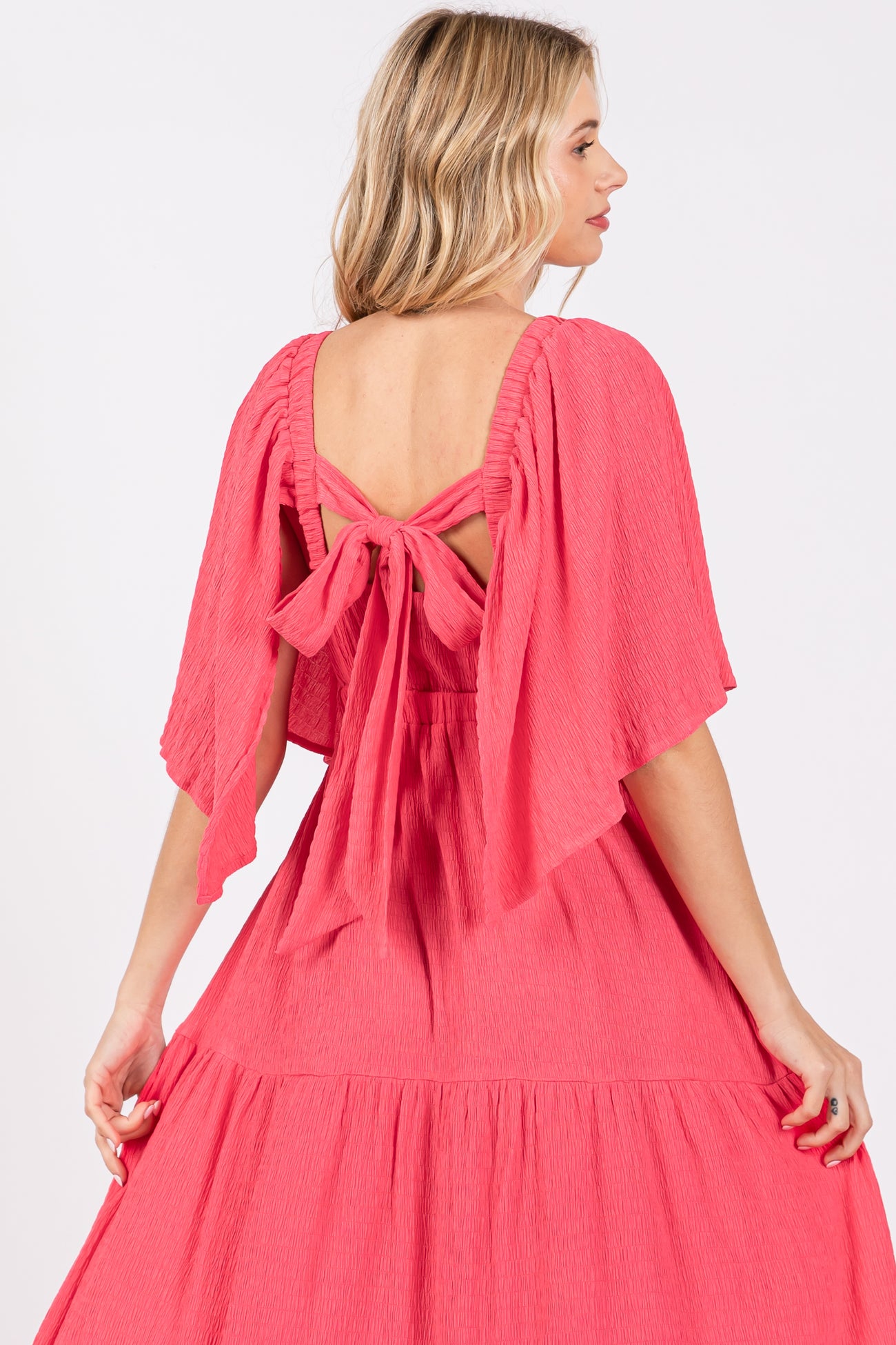 woman wearing a coral pink dress with short flutter sleeves and a tied back detail