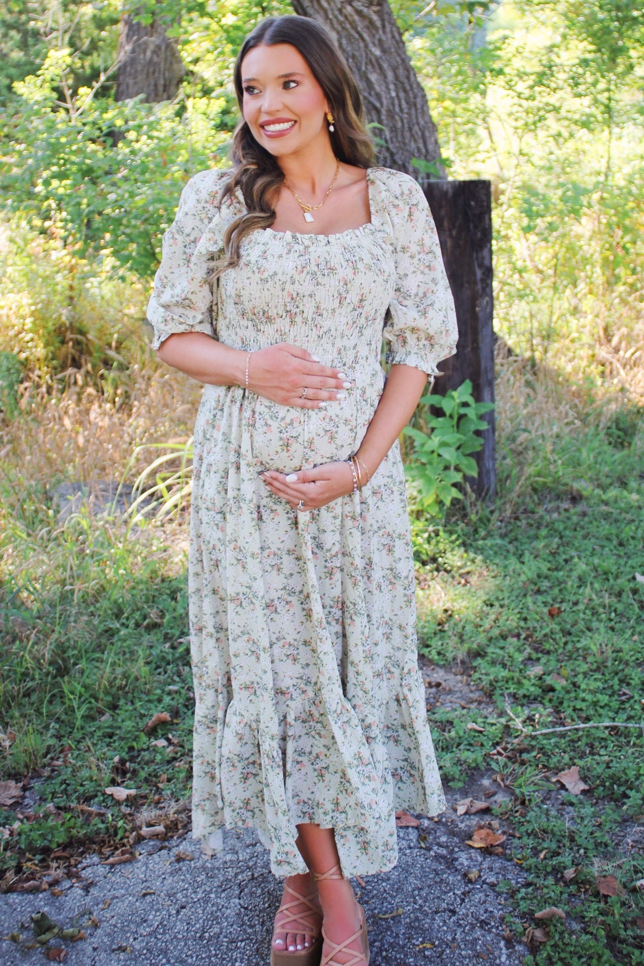 woman wearing a floral maternity dress with puff sleeves, standing outdoors and cradling her baby bump