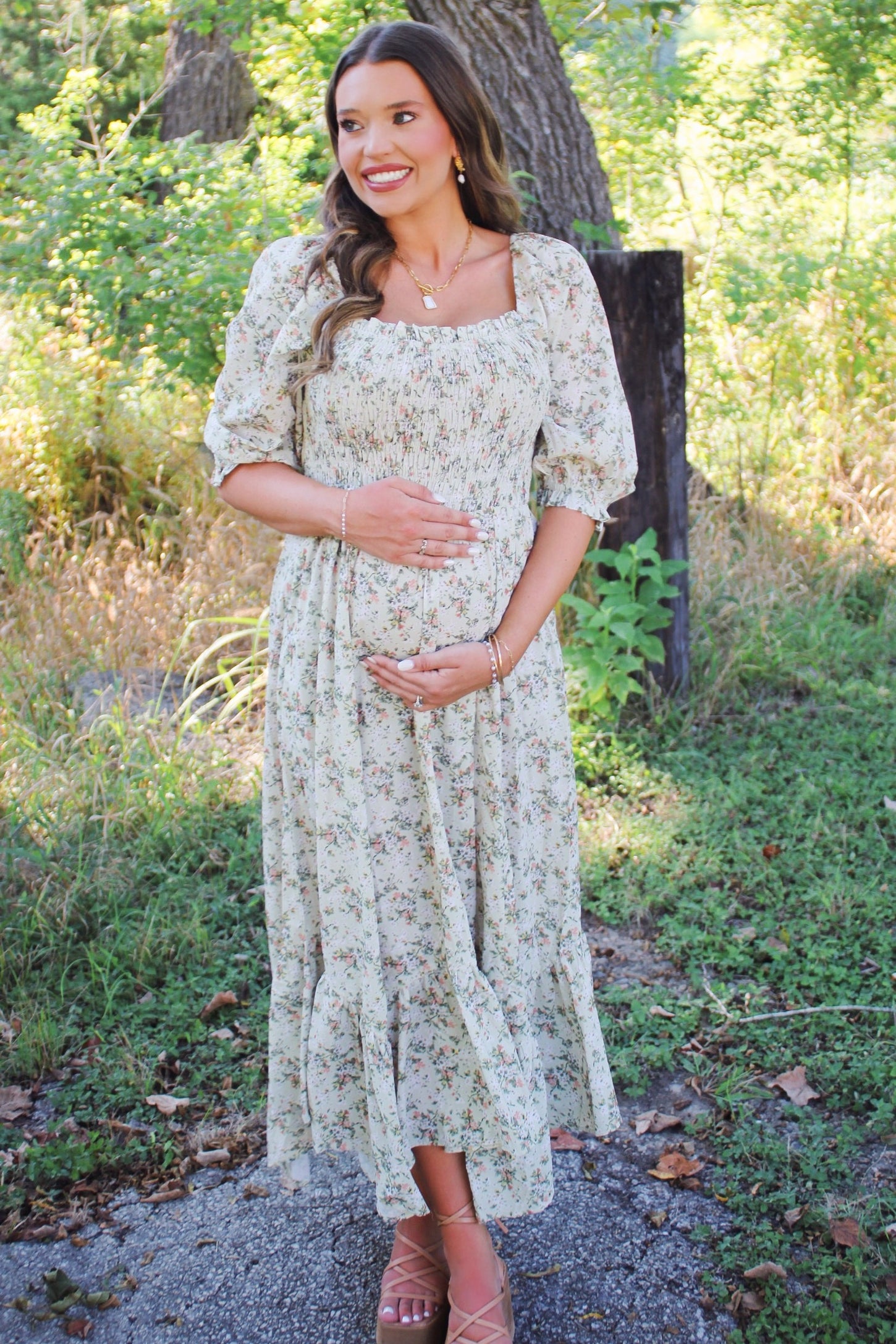 woman wearing a floral maternity dress with puff sleeves, standing outdoors and cradling her baby bump