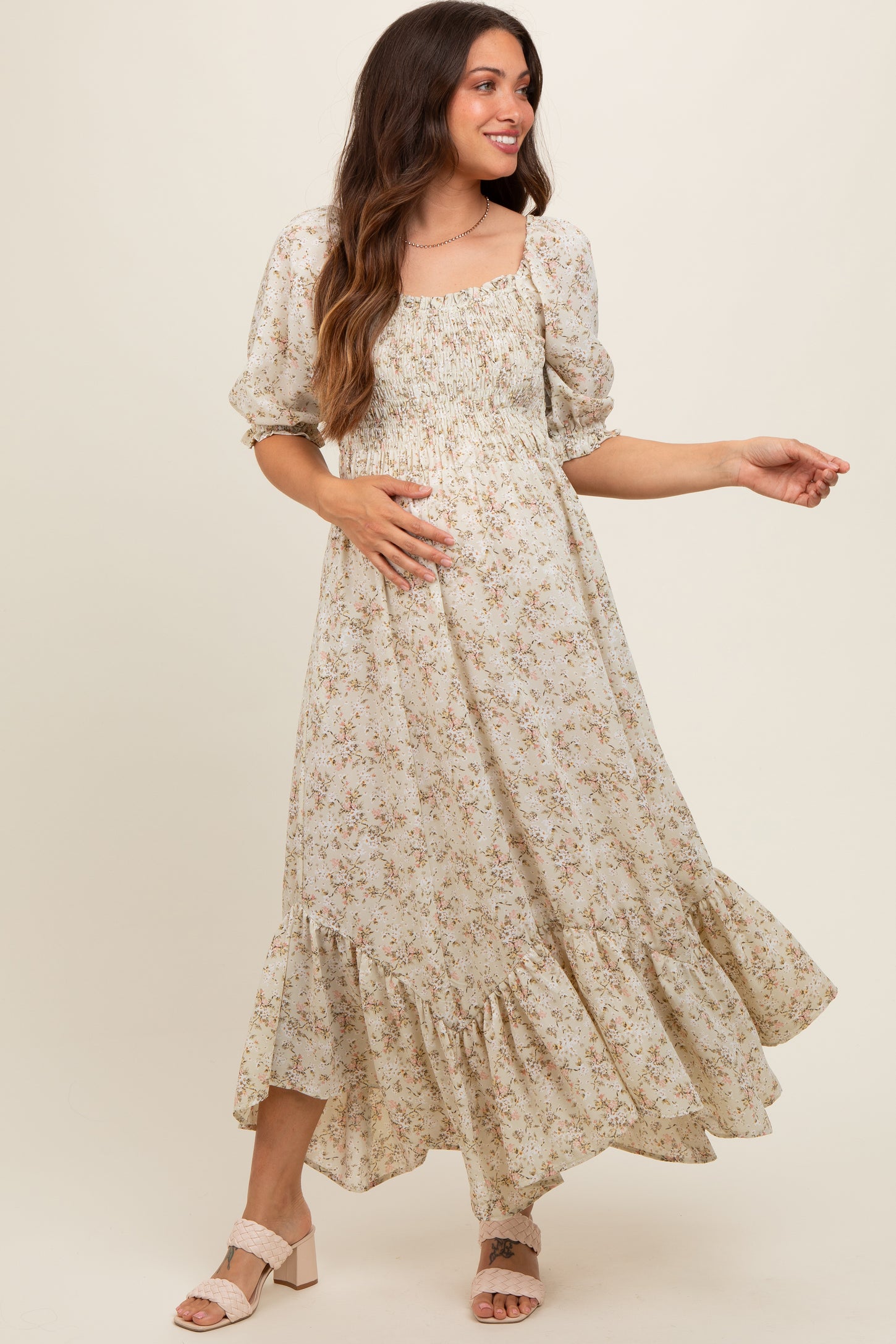 woman wearing a floral print maternity maxi dress with puff sleeves and a tiered hem, gently holding her baby bump