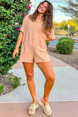 woman wearing a tan short sleeve romper with buttons and pockets, paired with wedge sandals and standing outside