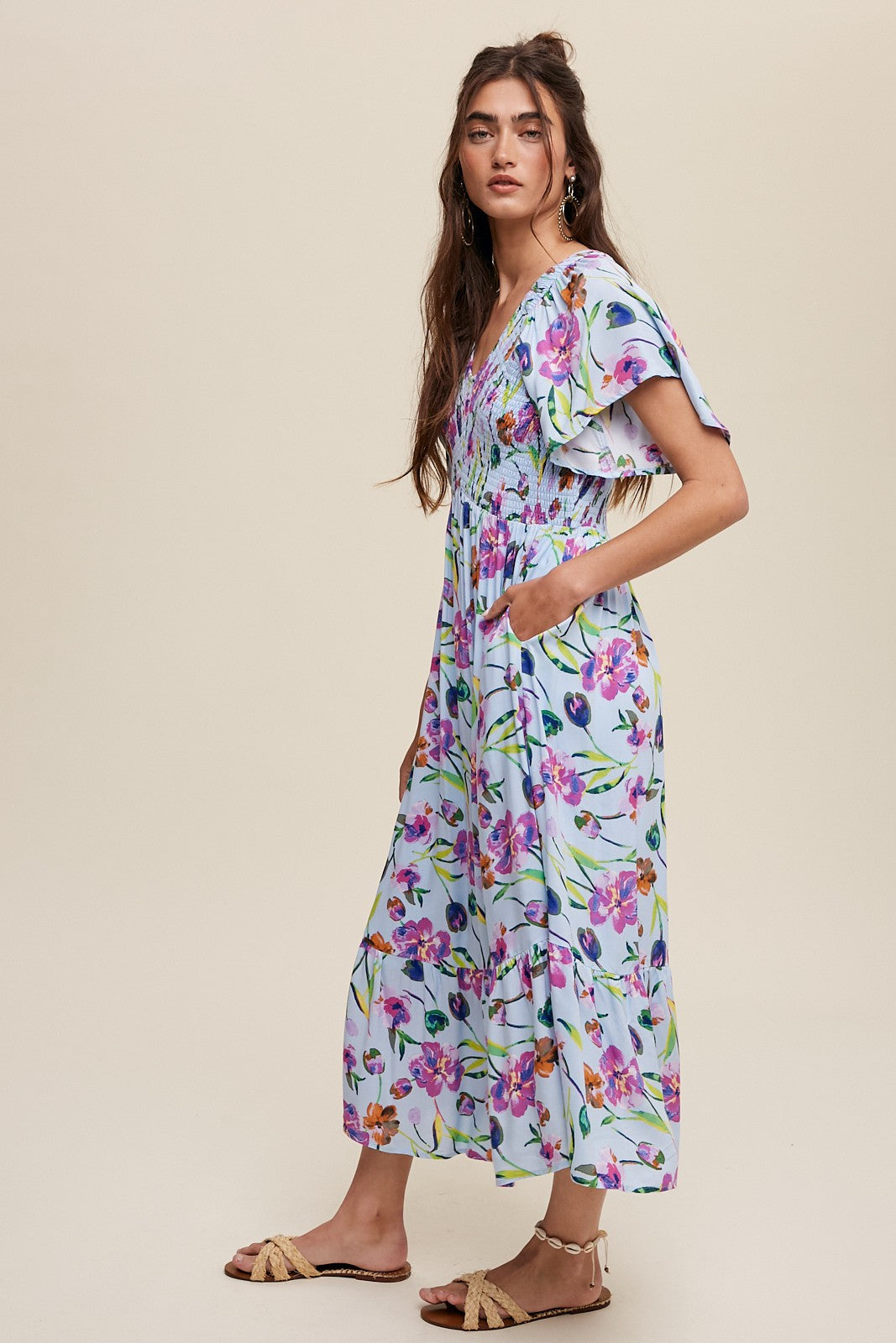 woman wearing a floral maxi dress with short flutter sleeves and pockets, standing against a light background